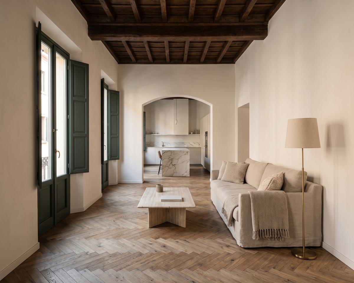 Soggiorno ristrutturato in un appartamento storico, con travi in legno a vista, parquet a spina e cucina con isola in marmo oltre l'arco